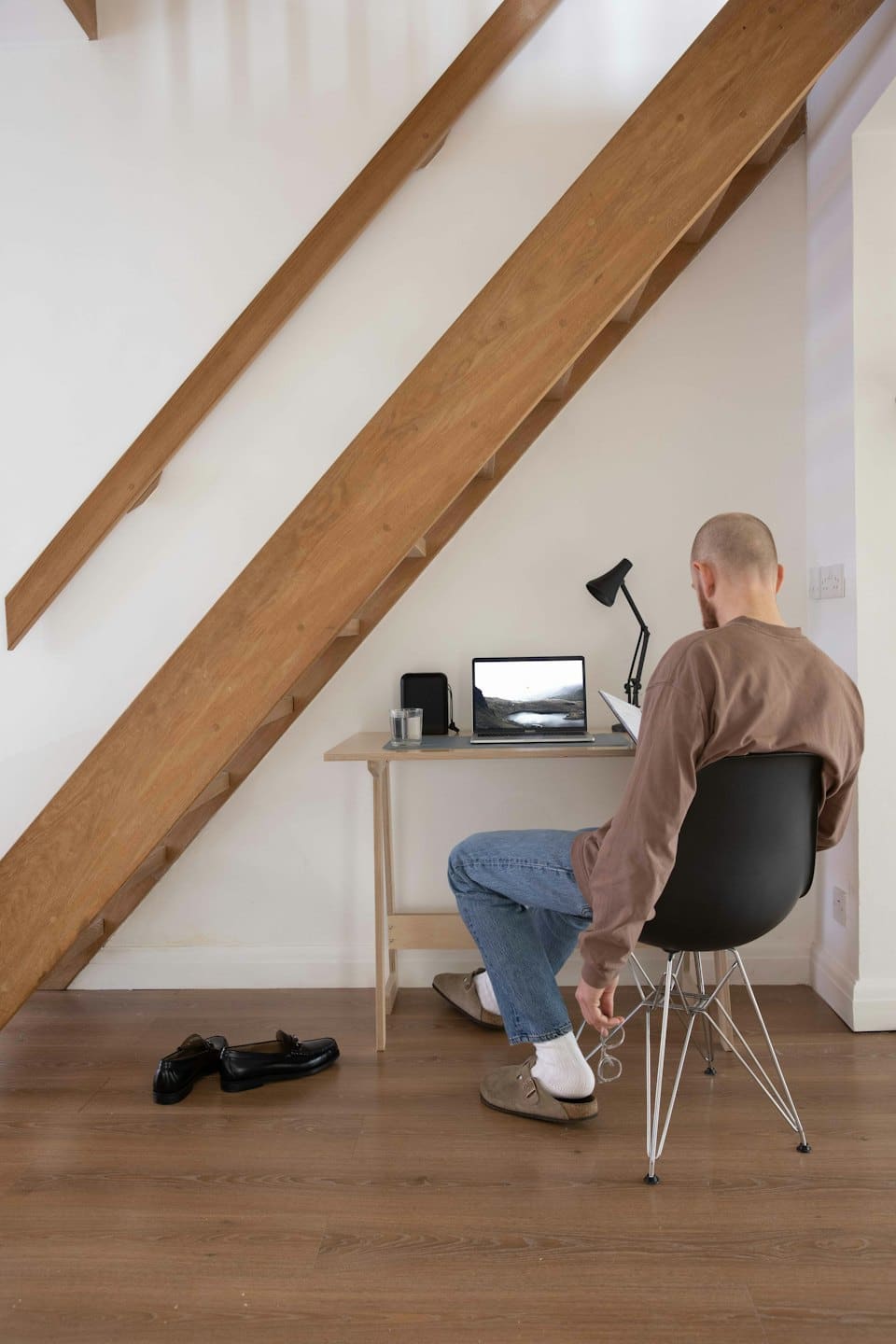 Man working on laptop at desk under staircase.