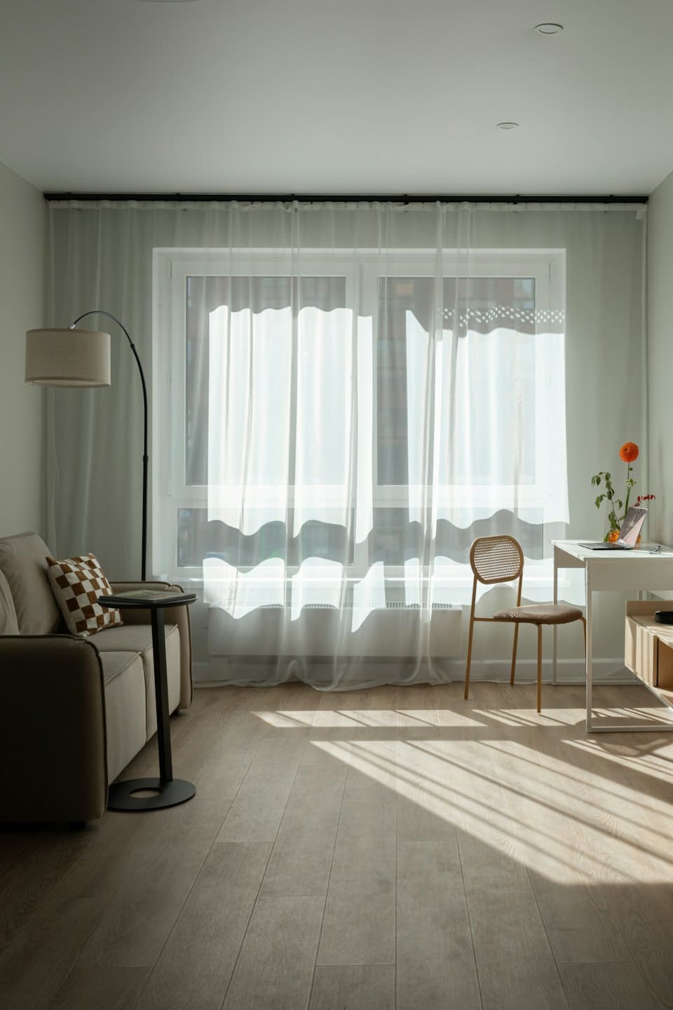 Modern living room with beige sofa, arc lamp, and desk with flowers.