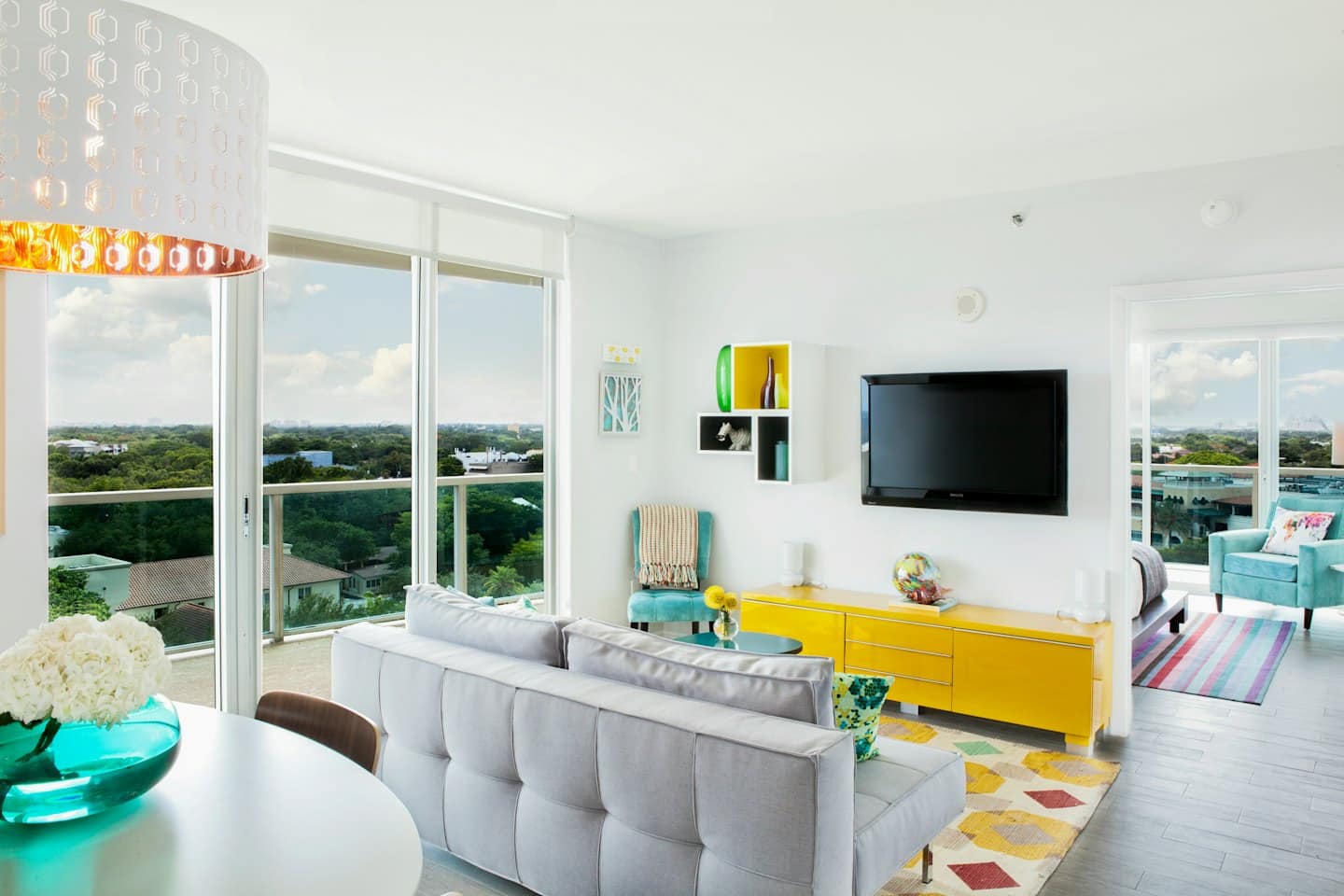 Modern living room with grey sofa and yellow media console overlooking city.