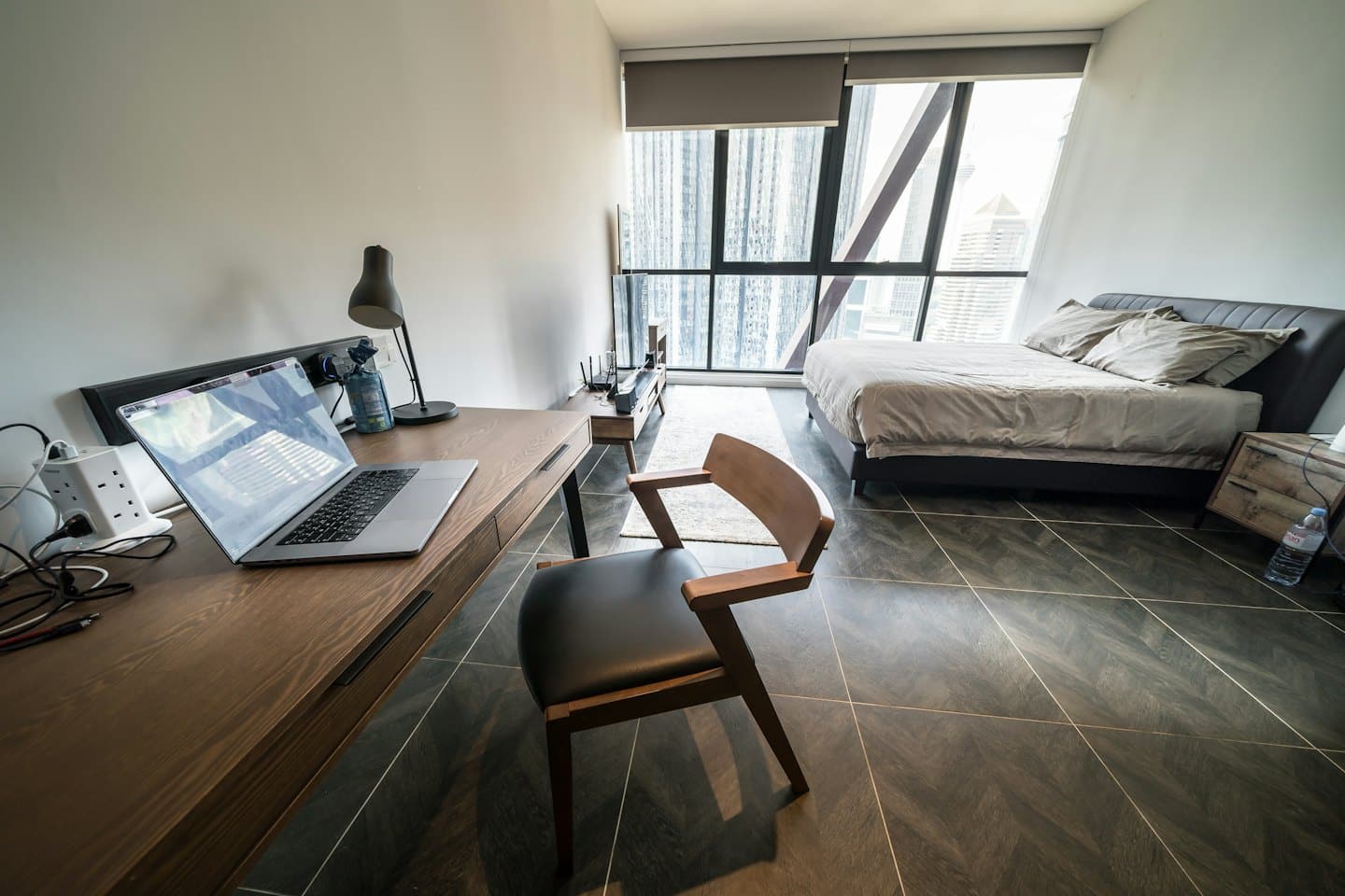 Modern studio apartment with a workspace and bed by city windows.